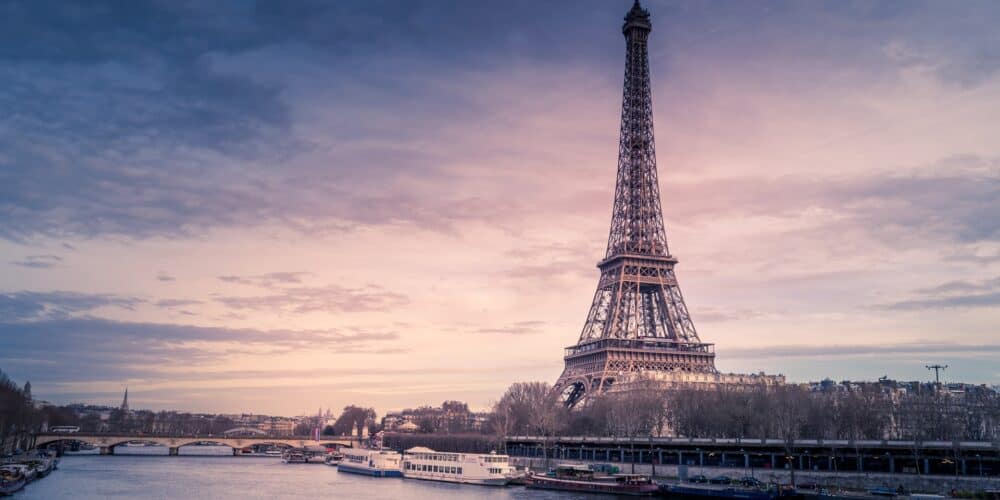 Eiffel Tower (a large metal tower) on the bank of a river at sunset