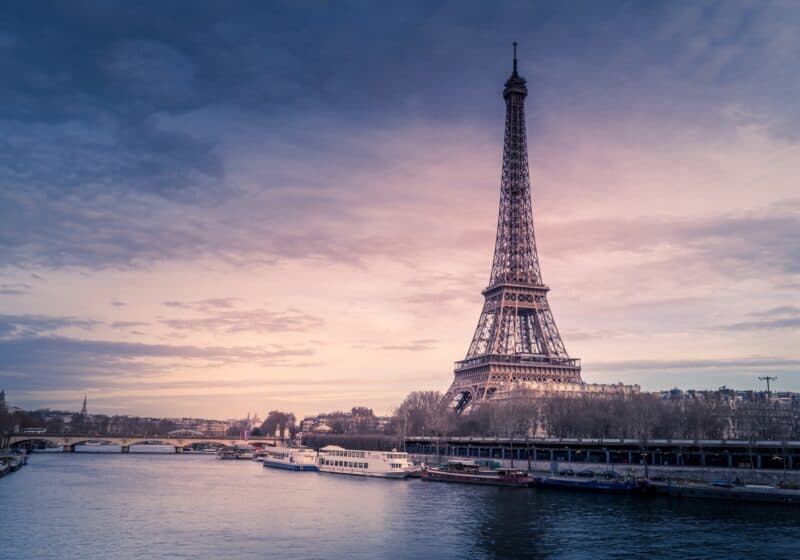 Eiffel Tower (a large metal tower) on the bank of a river at sunset