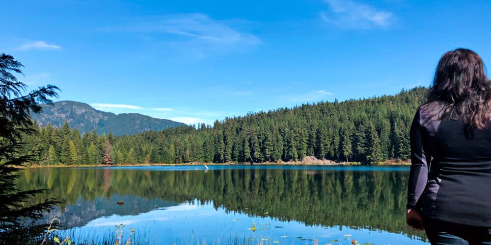 Girl staring out a lake surrounded by trees