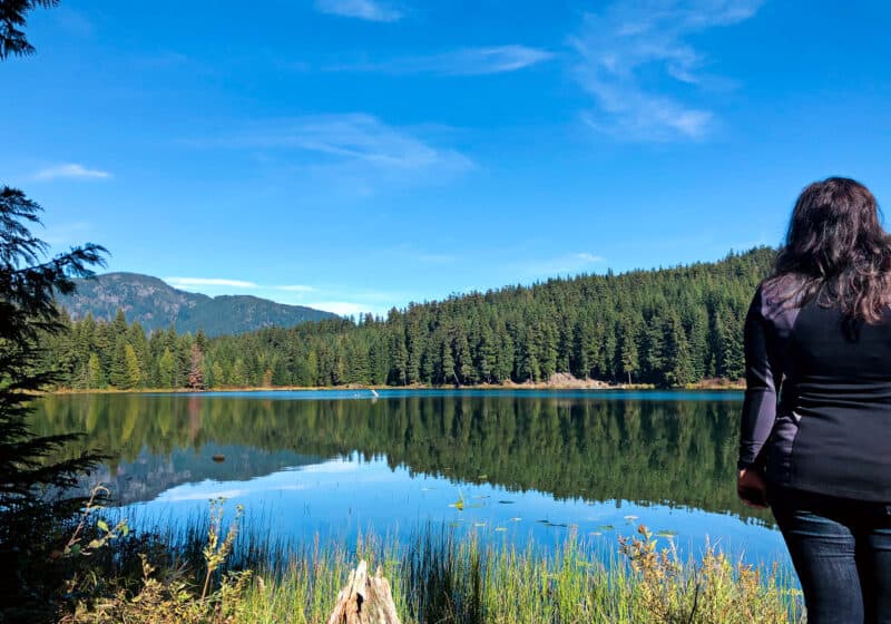 Girl staring out a lake surrounded by trees