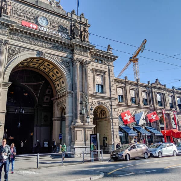Outside of Zurich trainstation, large stone building with columns in the front, and several Swiss flags