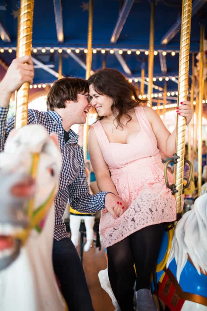 Boy and girl laughing and holding hands as the ride a carousel