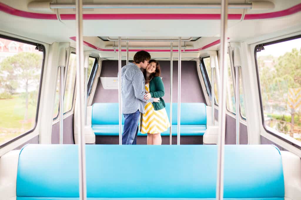 Boy and girl embracing and kissing in a brightly colored monorail car