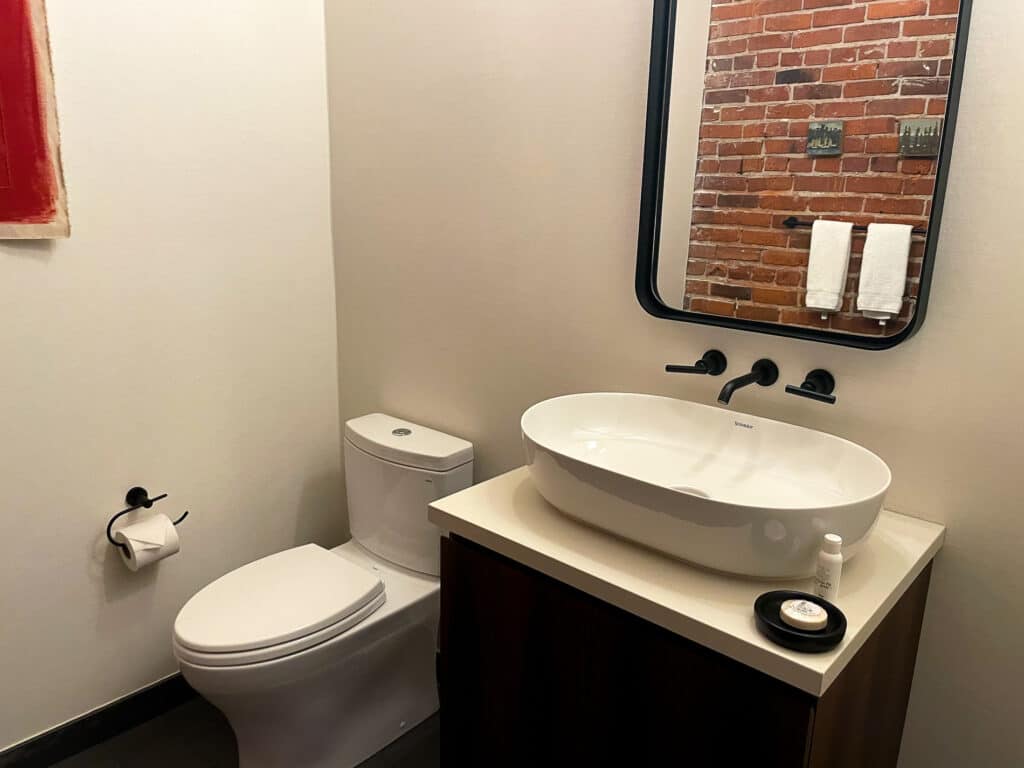 Alexis Hotel Half bathroom with toilet, sink, and brick wall