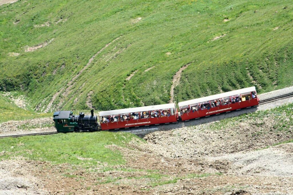 Top view of the green Brienz Rothorn Bahn engine pushing the red passenger car through the green swiss hillside