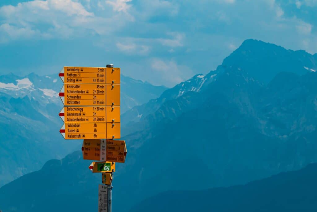 Orange directional sign pointing to different trails at the top of Brienz Rothorn with blue mountains in the background