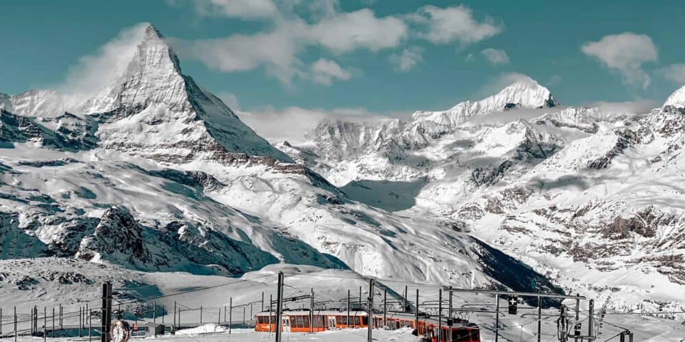 Red train running through a the snowy mountains with the tall Matterhorn peak in the background