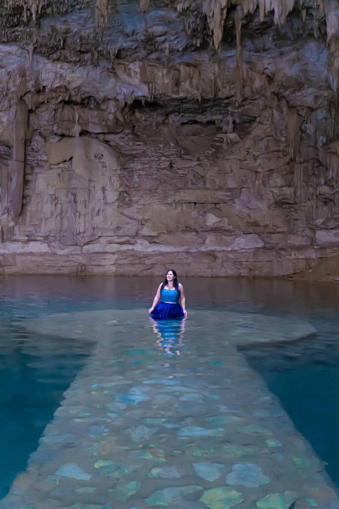 Girl in blue standing on a water covered platform inside a cave / cenote
